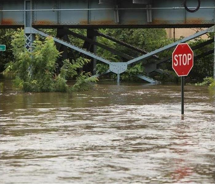 Flooded streets with a bridge and stop sign to the right. 