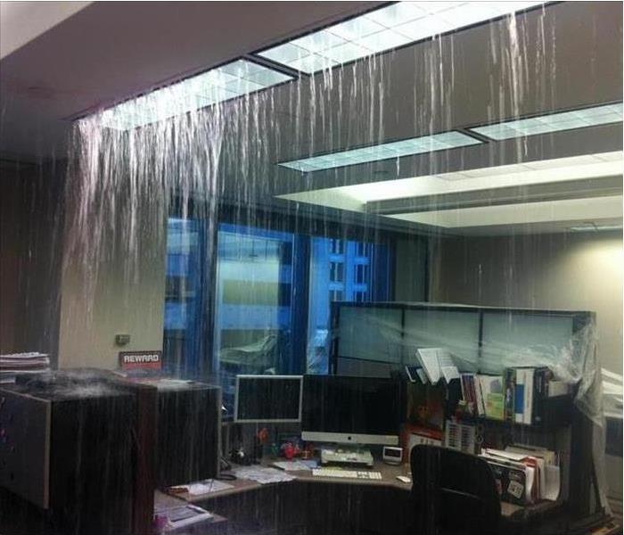 Water pours from a ceiling light fixture in an office