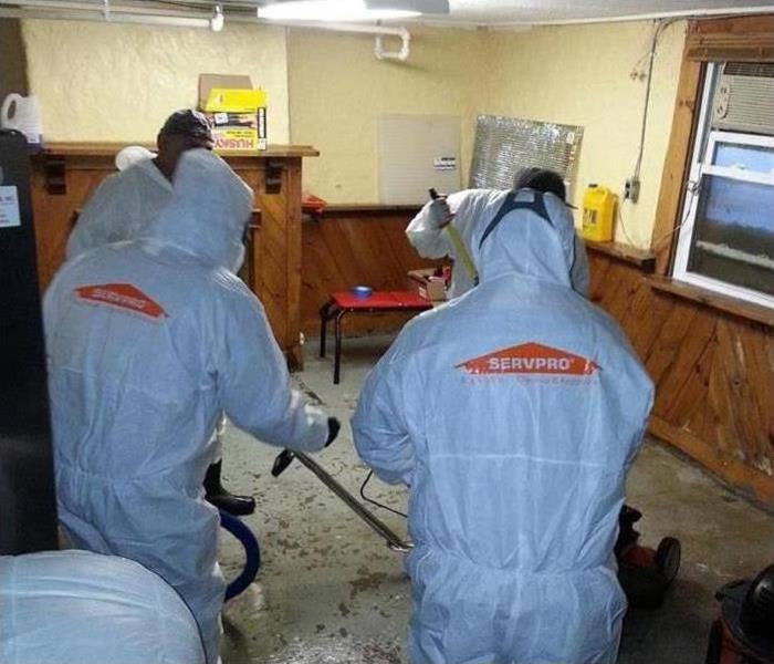 Workers in hazmat suits clean a biohazard-contaminated workplace.